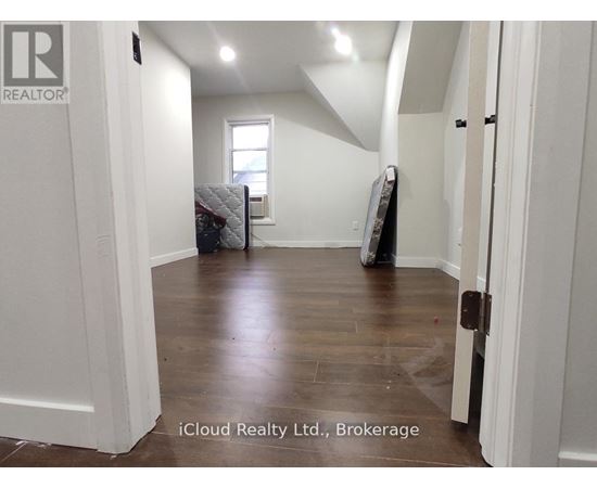 A room with white walls and wooden flooring, with a mattress and box spring in the corner.