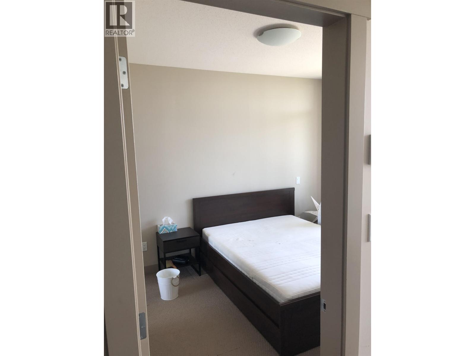 A bedroom with a bed, nightstand, and cup on the floor.