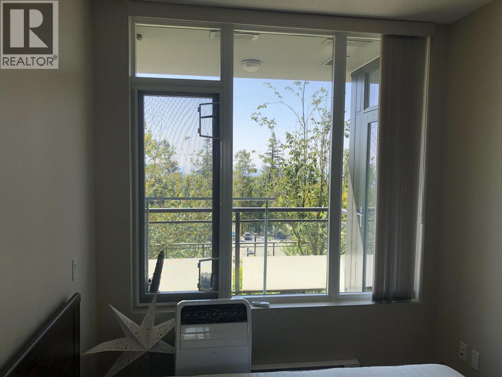 A bedroom with a bed, a window with a view of a fence and trees, and a washing machine.
