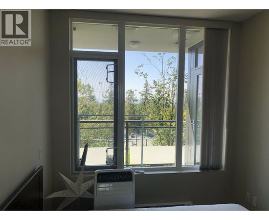 A bedroom with a bed, a window with a view of a fence and trees, and a washing machine.