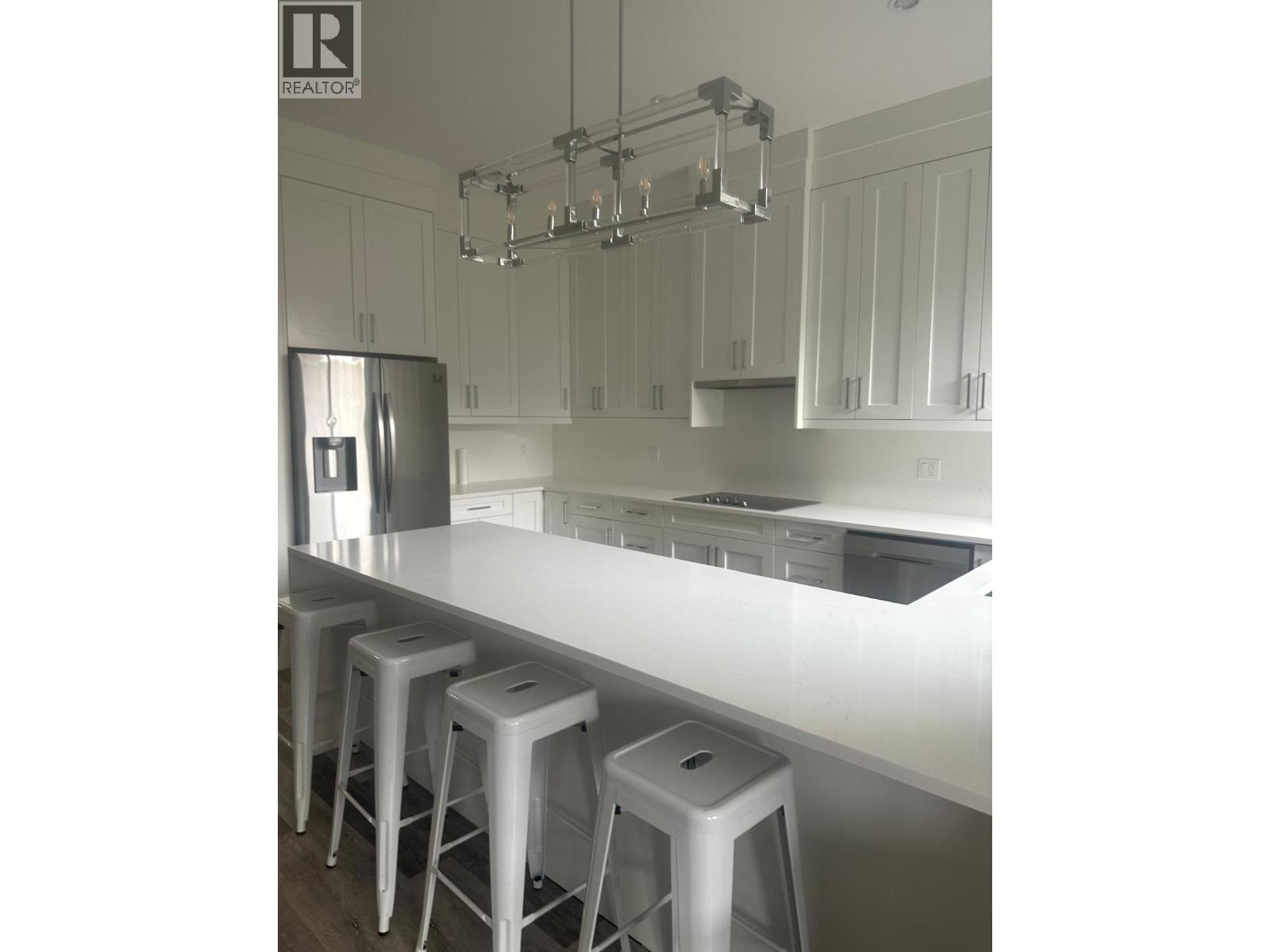 A kitchen with white cabinets and a white island with three stools.