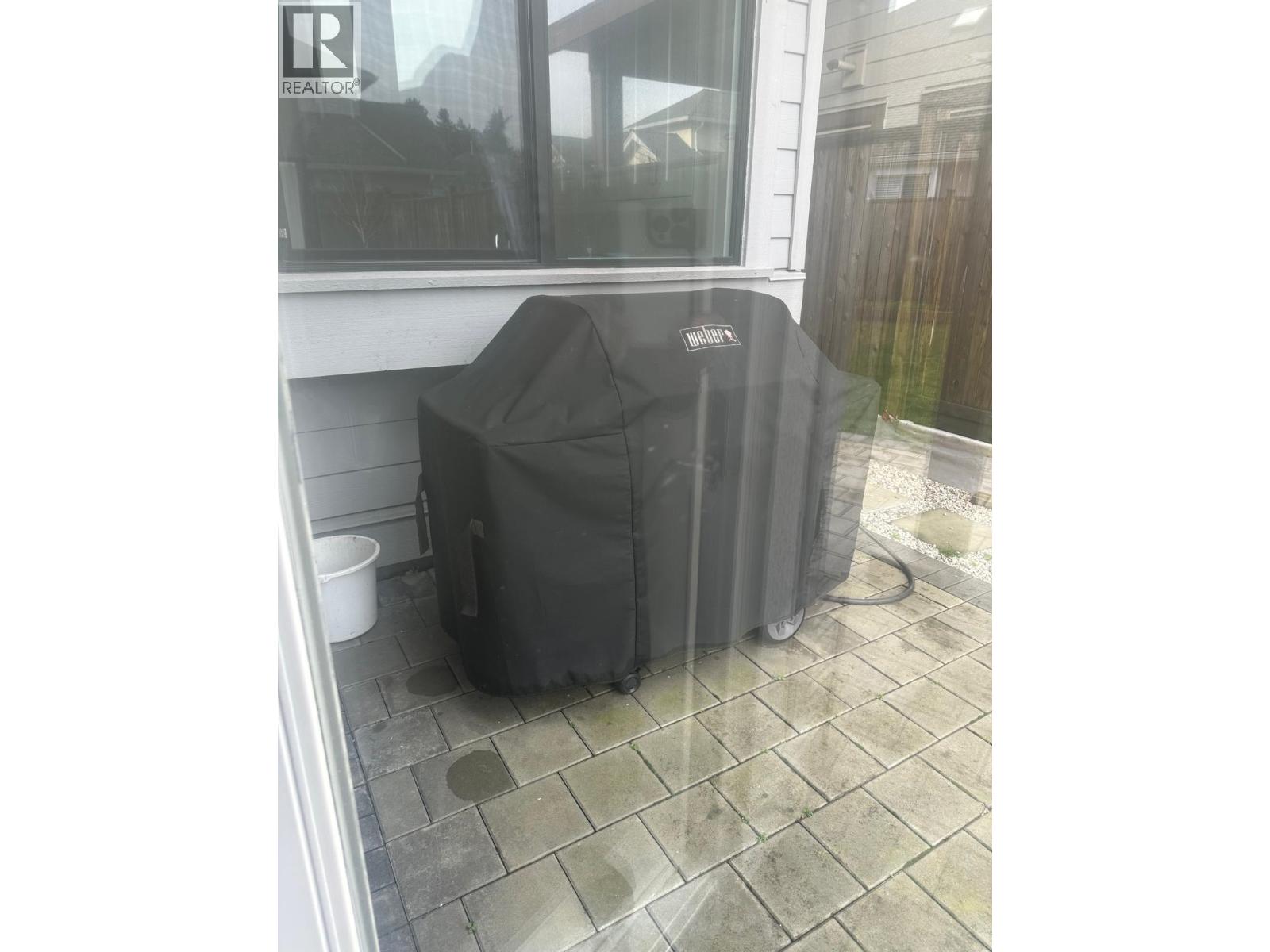 A black covered grill is on a patio outside a Realty building.
