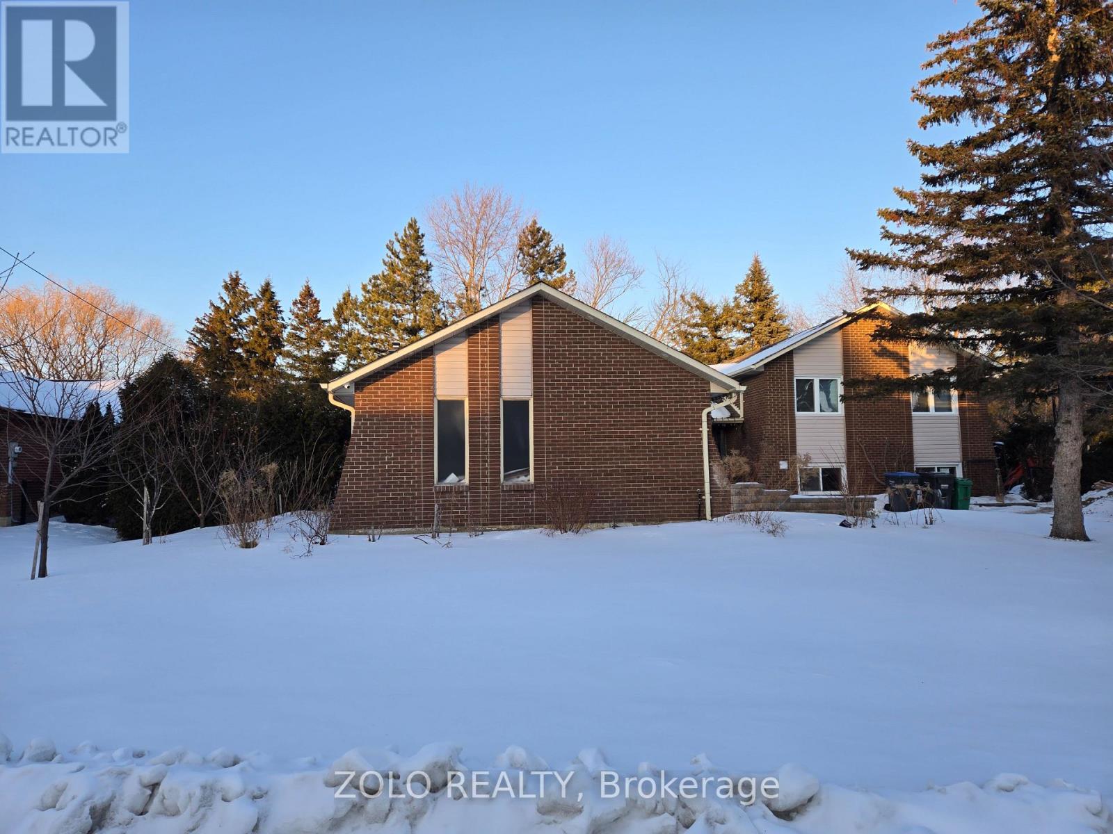 A house with a snowy front yard and trees in the background.