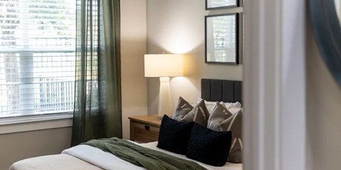 A bedroom with a bed, nightstand, and a window with curtains.