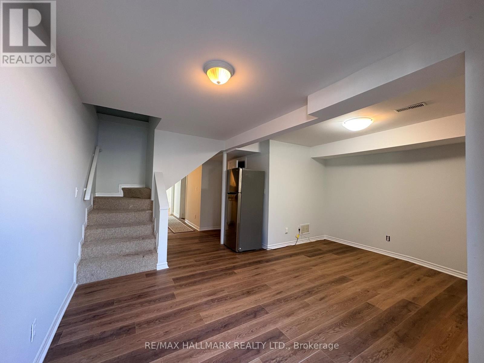A spacious room with wooden flooring and a staircase leading to another room.