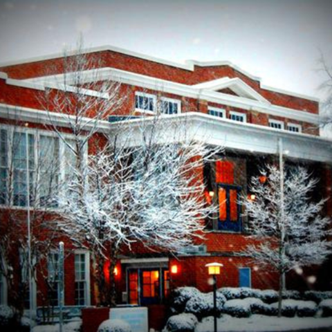 A red building with snow on the ground and trees.