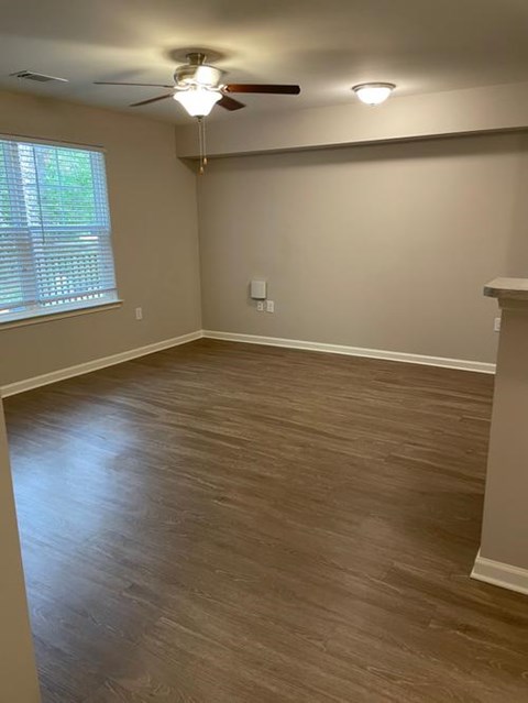 A room with a ceiling fan and light, wooden flooring, and a window with blinds.