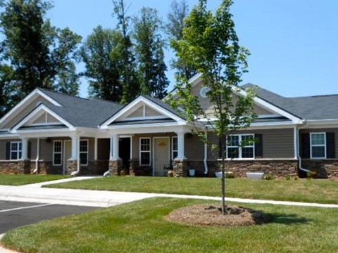 A house with a grey roof and white trim is surrounded by a grassy lawn.