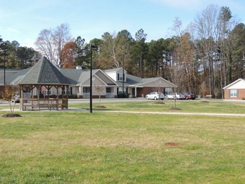 A gazebo is in the middle of a grassy area in front of a house.
