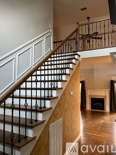 A staircase with a wooden handrail and black balusters leads to a living room with a fireplace.