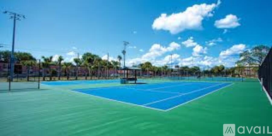 A tennis court with a blue surface and white lines, surrounded by a fence and trees.