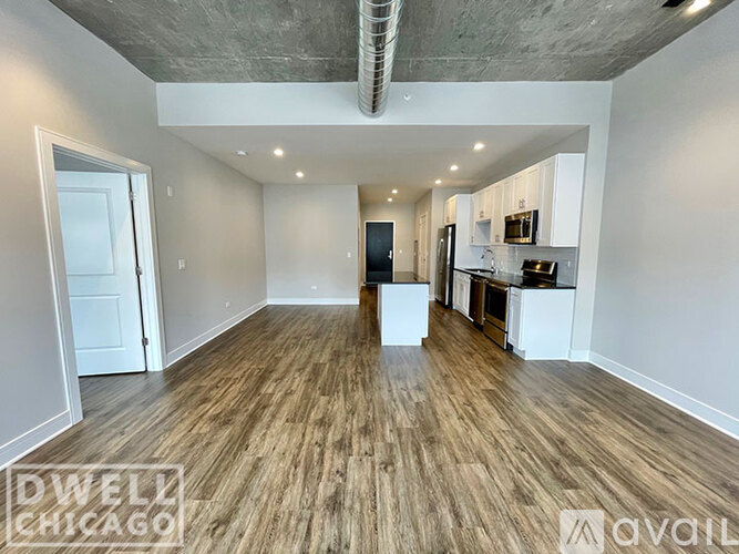 A spacious room with wooden flooring and a kitchen area in the background.