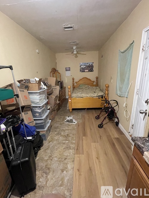 A room with a bed, a fan, and a lot of boxes on the floor.