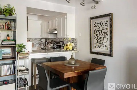 A dining room with a wooden table and chairs, a bookshelf, and a framed artwork on the wall.