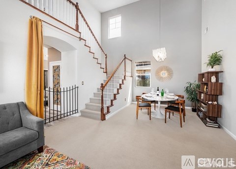 A living room with a grey couch, a dining table with chairs, a staircase with a railing, and a potted plant.