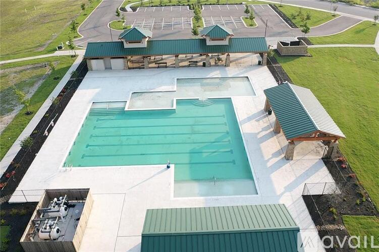 An aerial view of a swimming pool surrounded by a green roofed building and a parking lot.