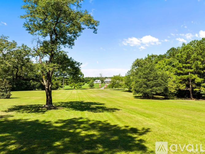 A tree stands in a grassy field with a house in the distance.