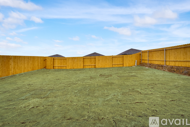 A large, empty yard with a wooden fence and a grassy field.
