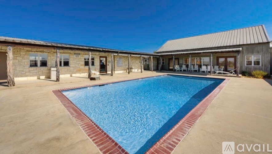 A large outdoor swimming pool is surrounded by a building and lounge chairs.