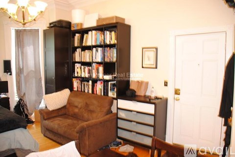 A living room with a brown leather couch and a bookshelf filled with books.