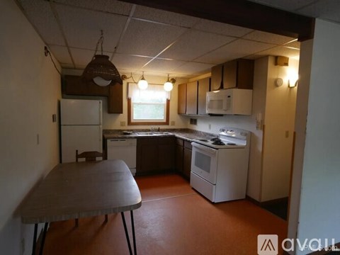 A kitchen with a table and chairs in the foreground and a refrigerator, microwave, oven, and stove in the background.