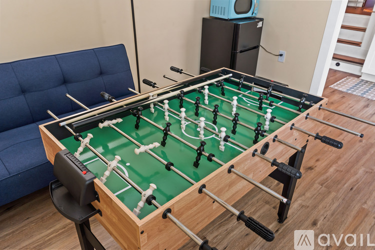A foosball table sits in a living room with a blue couch and a TV in the background.
