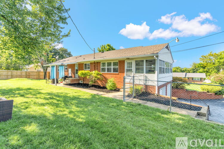 A house with a blue door and a red brick exterior is surrounded by a green lawn and a chain link fence.