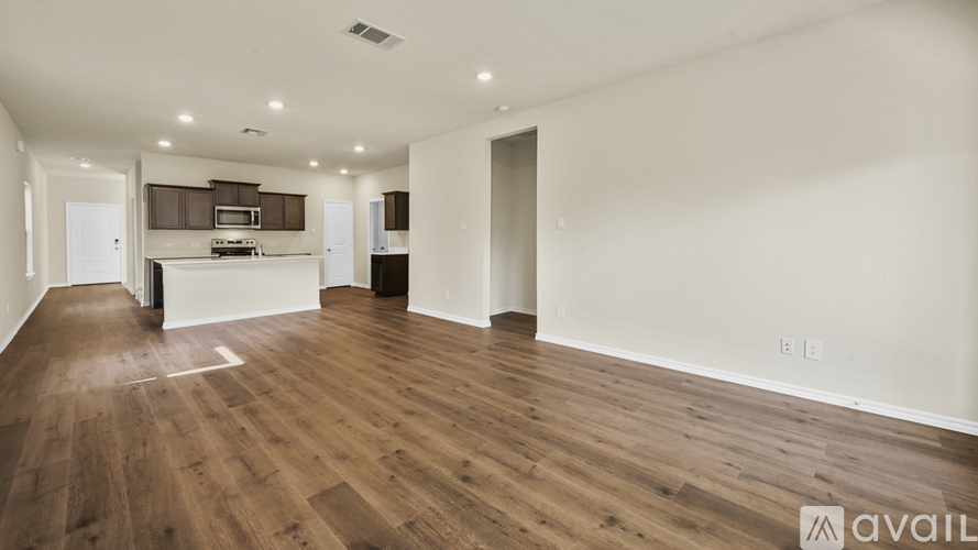 A spacious living room with hardwood floors and a kitchen in the background.