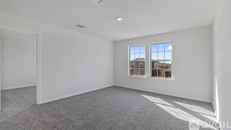A spacious room with a carpeted floor, a window with a view of buildings outside, and a door leading to another room.