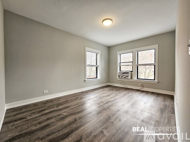 A room with wooden flooring and two windows.