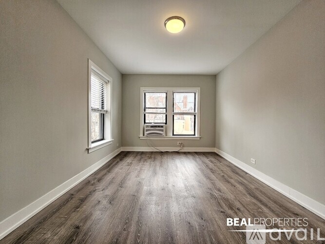 A spacious room with wooden floors and two windows.