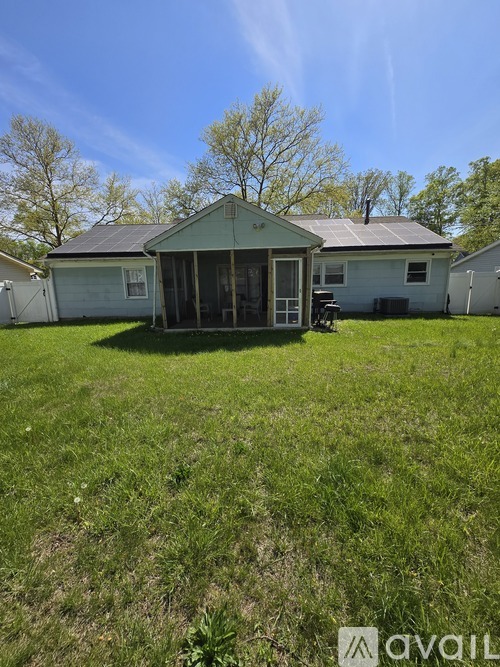A house with a green roof and a porch is surrounded by a grassy yard.