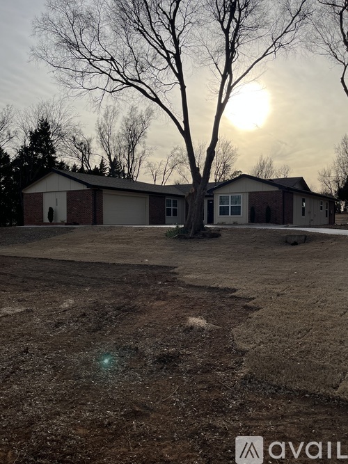 A house with a tree in front of it and the sun setting in the background.