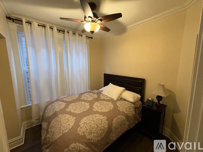 A bedroom with a bed, a ceiling fan, and a window with curtains.