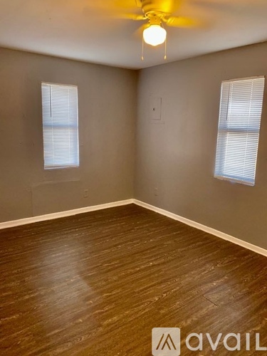 A room with wooden flooring and two windows.