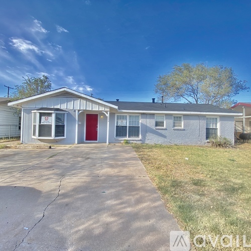 A small house with a red door is surrounded by a grassy area and a clear sky.