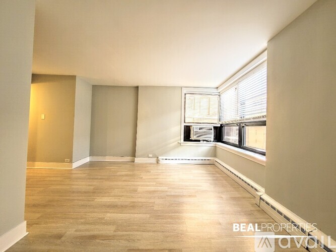A spacious room with wooden flooring and a window with blinds.