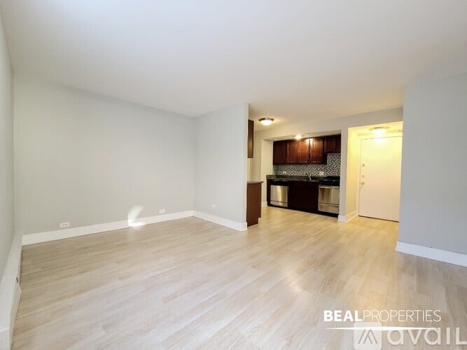 A spacious room with wooden flooring and a kitchen area in the background.