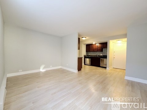 A spacious room with wooden flooring and a kitchen area in the background.
