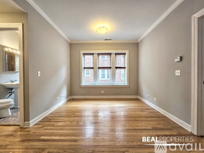 A spacious room with wooden floors and a window with blinds.