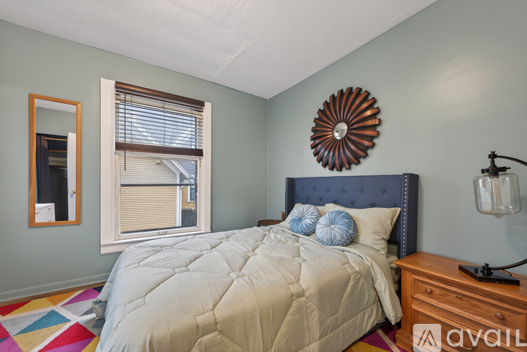 A bedroom with a bed, dresser, and a window with blinds.