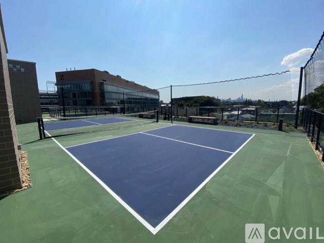 A tennis court with a blue surface and white lines, surrounded by a fence and a building in the background.