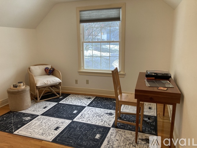 A room with a chair, a table, and a quilt on the floor.