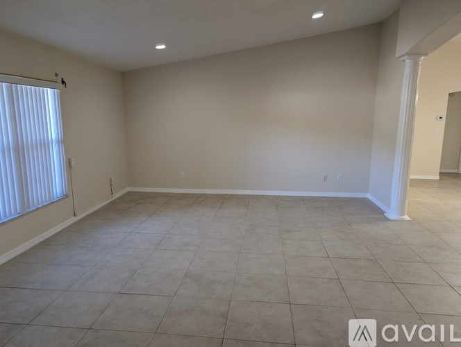 A spacious room with tiled flooring and a window with blinds.