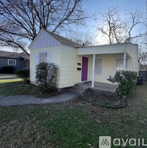 A small house with a purple door is surrounded by a grassy area and a tree.