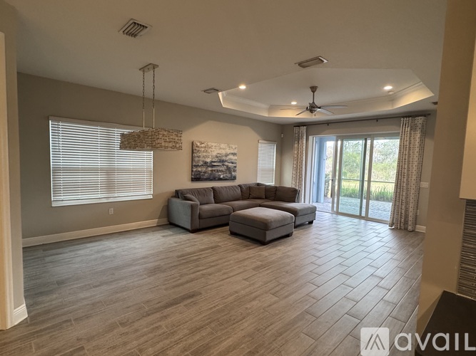 A spacious living room with a grey sofa set and a large window with blinds.