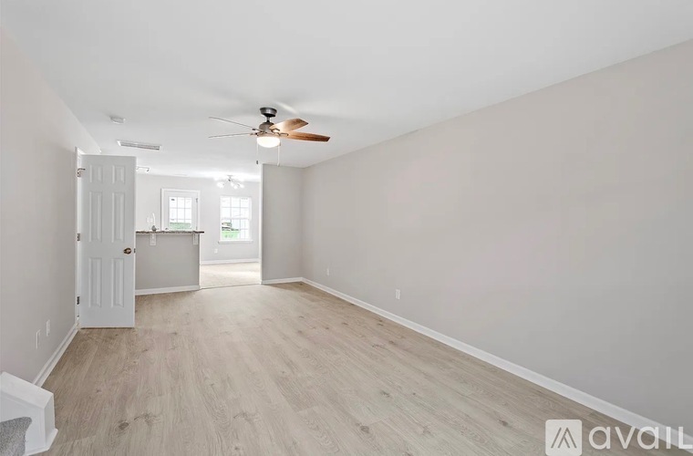 A spacious room with a ceiling fan and light, hardwood flooring, and a door leading to another room.