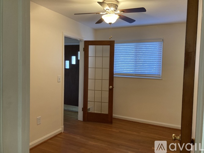 A room with a ceiling fan and a door leading to a darker room.