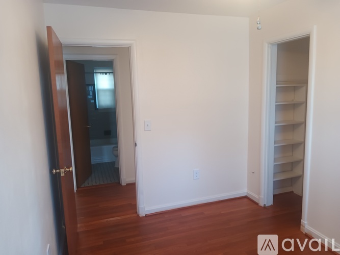 A room with a wooden floor and white walls, with a door on the left and a closet on the right.