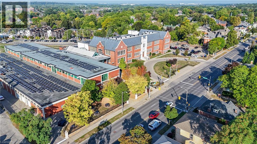 A large building with a green roof is surrounded by trees and a road with cars.